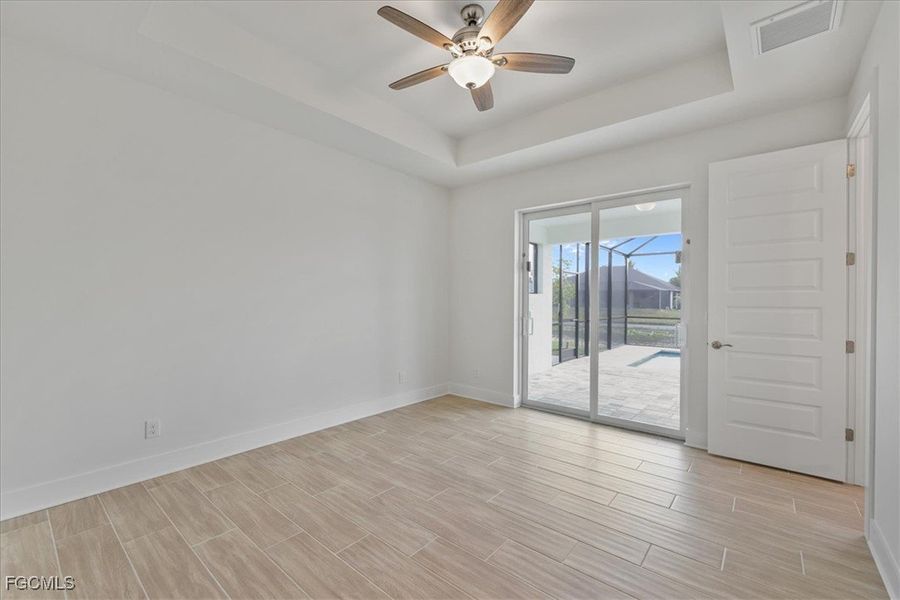 Empty room with a tray ceiling, ceiling fan, and wood tiled floors