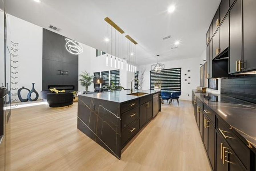 Modern kitchen featuring dark cabinetry with gold-tone hardware, black subway tile backsplash, and light wood-finish flooring