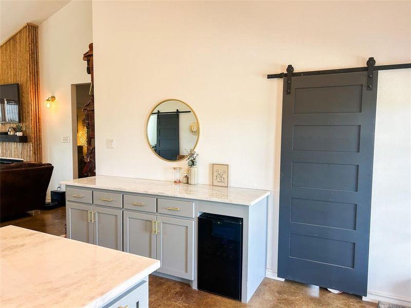Bar featuring gray cabinetry, light stone countertops, a barn door, and black refrigerator Bar featuring gray cabinetry, light stone countertops, a barn door, and black refrigerator