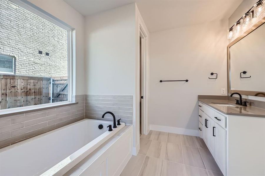 Bathroom featuring tile patterned flooring, vanity, tasteful backsplash, and a tub