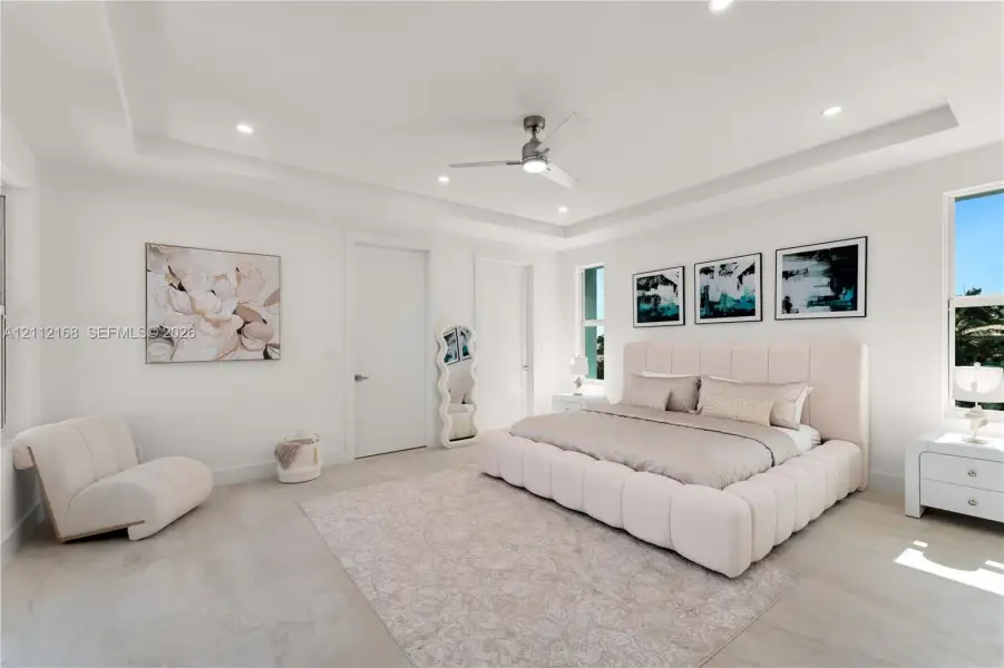 Spacious interior featuring a tray ceiling, recessed lighting, neutral large-format tile flooring, and a modern ceiling fan Spacious interior featuring a tray ceiling, recessed lighting, neutral large-format tile flooring, and a modern ceiling fan