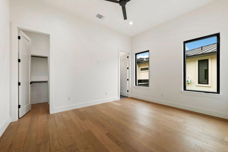 Spacious room featuring wood-finish flooring, white walls, and a black ceiling fan