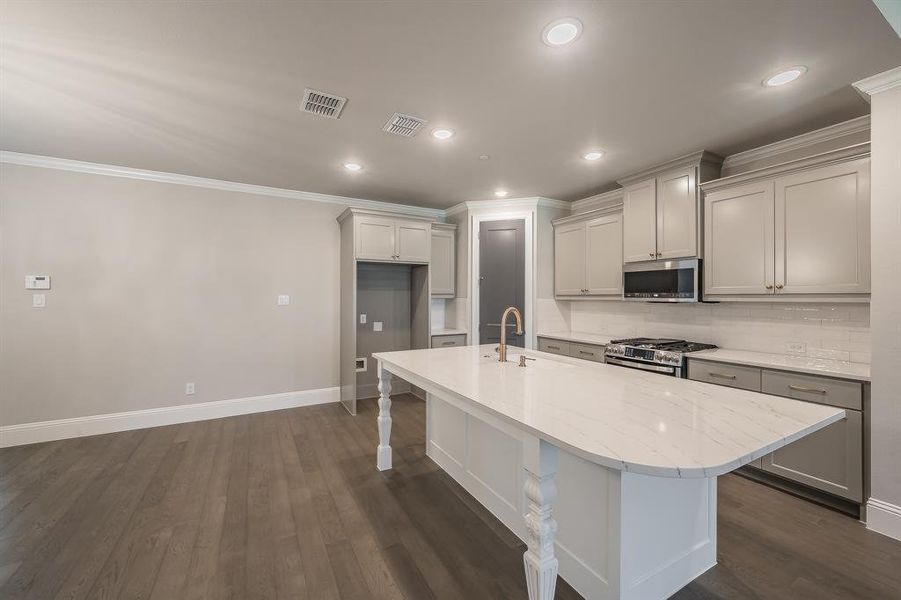 Kitchen featuring a large central island with a stone countertop, a gold-finish faucet, and turned leg accents
