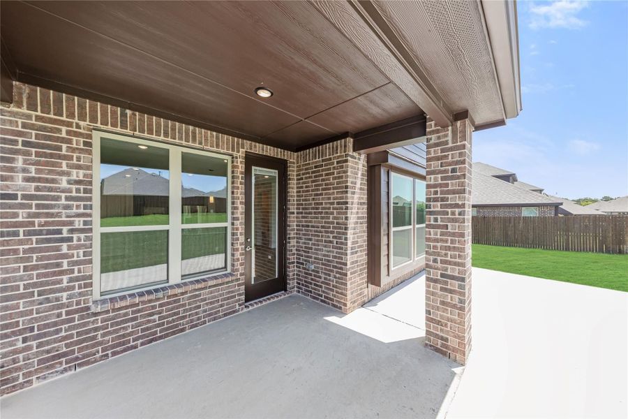 Covered back patio with brick exterior, wood ceiling, and concrete slab overlooking fenced backyard