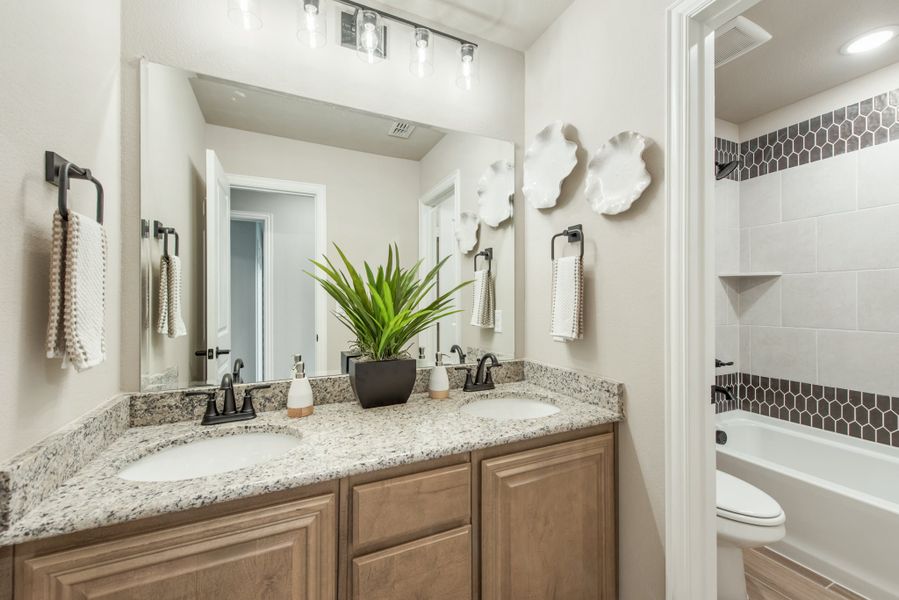 Bathroom with double sink vanity, granite countertop, wood cabinets, and tiled shower-tub combo with dark accent tiles.