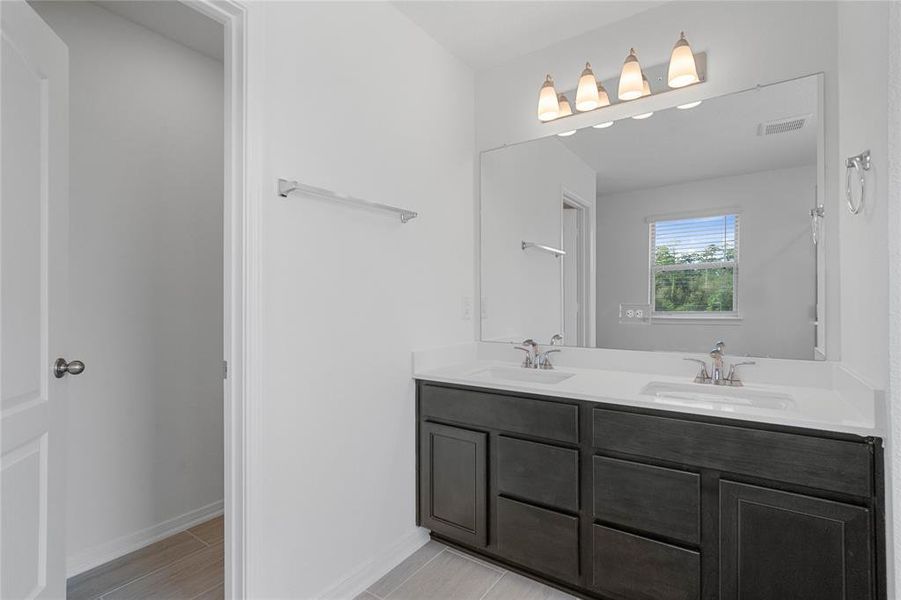 This primary bathroom is definitely move-in ready! Featuring an oversized tub and walk-in shower with tile surround, stained cabinets with light countertops, dual vanities, high ceilings, neutral paint, sleek and modern finishes.