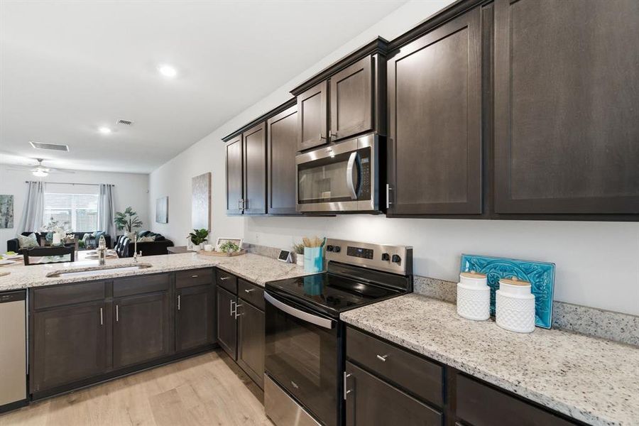 The kitchen features dark wood cabinetry, light-colored granite countertops, and stainless steel appliances including an oven and microwave