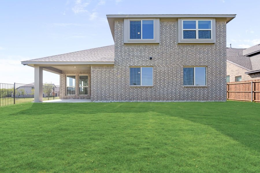 Two-story brick home rear view with covered patio, large green backyard, and fenced yard