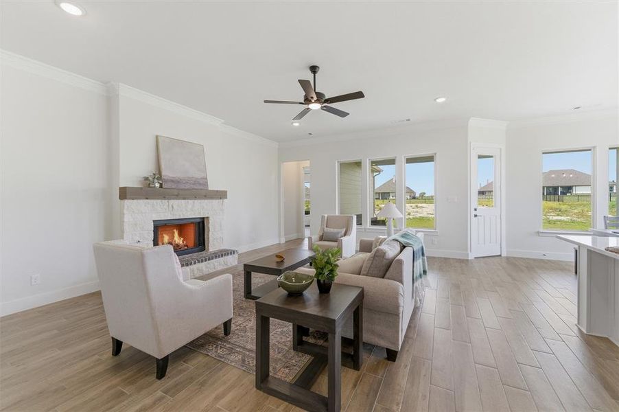 Spacious living area featuring a stone fireplace with a wood mantle, wood-finish flooring, a ceiling fan, recessed lighting, and multiple windows