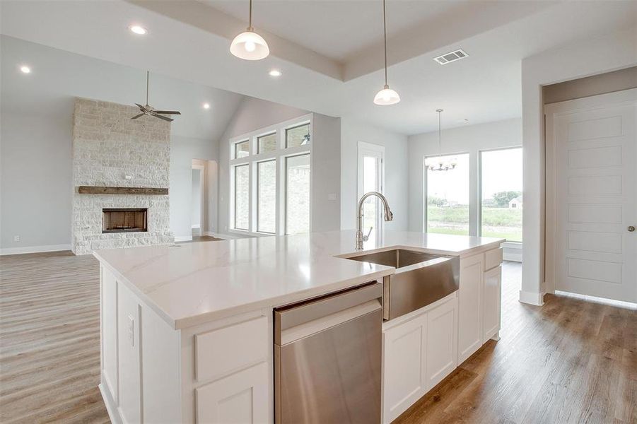 Kitchen featuring a center island with sink, a fireplace, stainless steel dishwasher, and wood-type flooring