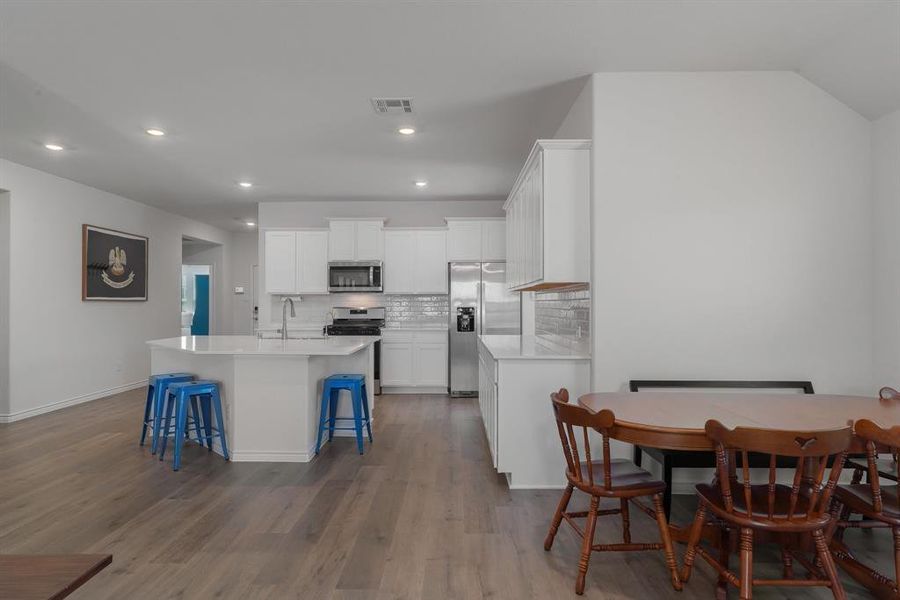 Kitchen with a breakfast bar area, a kitchen island with sink, stainless steel appliances, visible vents, and tasteful backsplash