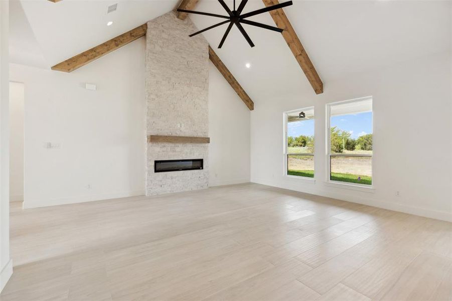 Unfurnished living room with a fireplace, ceiling fan, light wood-type flooring, high vaulted ceiling, and beamed ceiling