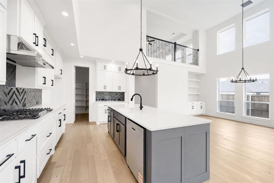 Modern kitchen featuring white cabinetry, black hardware, stainless steel appliances, a gray island with a white countertop, and herringbone tile backsplashes