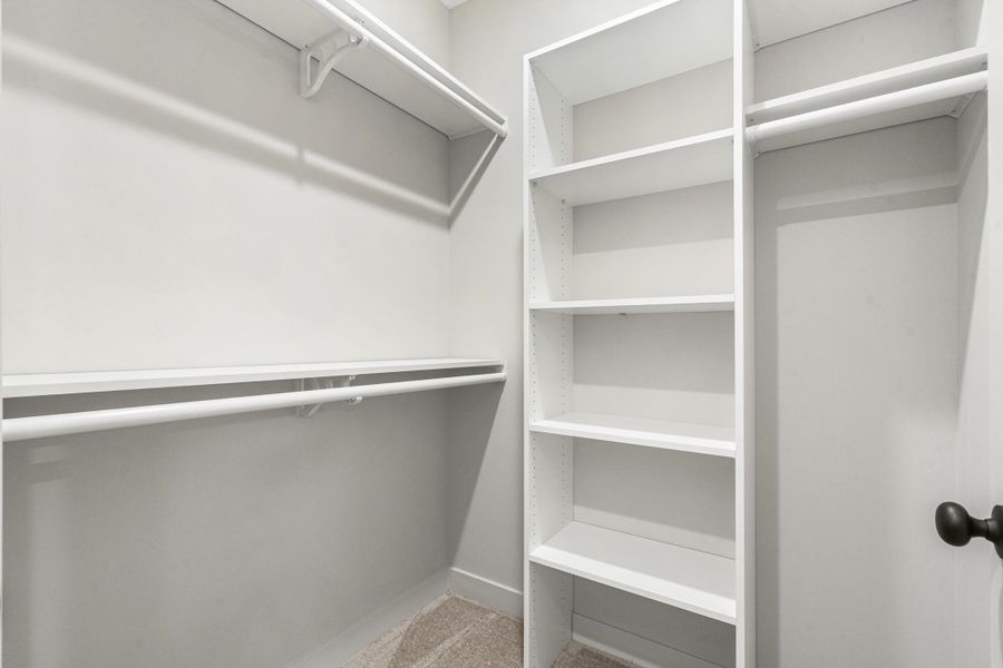 Walk-in closet featuring white built-in shelving, multiple hanging rods, and light-colored carpet flooring Walk-in closet featuring white built-in shelving, multiple hanging rods, and light-colored carpet flooring