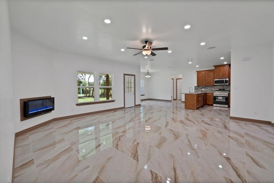 Unfurnished living room with recessed lighting, a glass covered fireplace, a ceiling fan, and light marble finish flooring