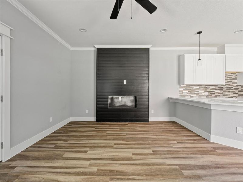 Unfurnished living room featuring ceiling fan, a large fireplace, crown molding, baseboards, and light wood finished floors