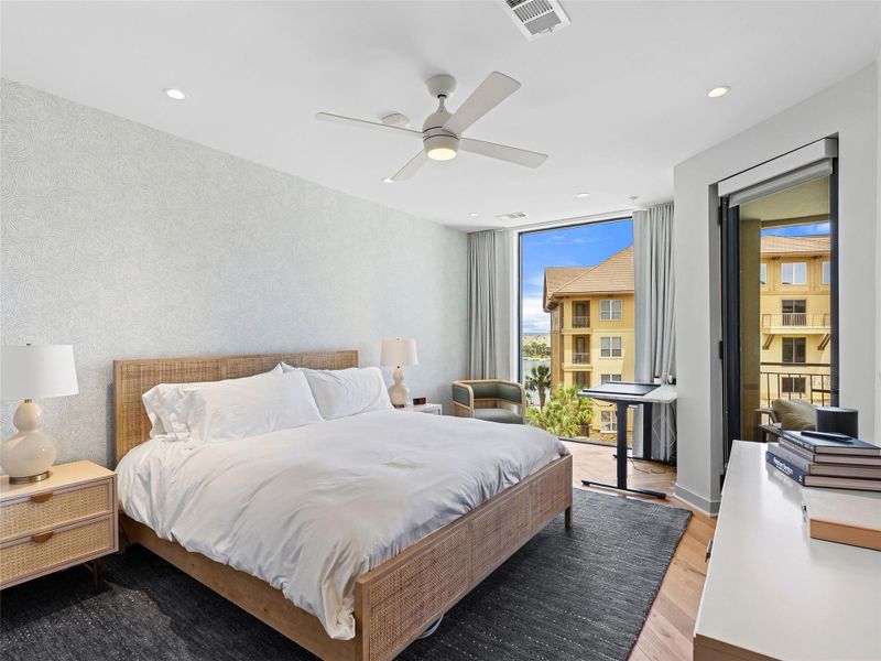 Light-filled bedroom featuring floor-to-ceiling windows, recessed lighting, and a ceiling fan and a peak at the lake. Light-filled bedroom featuring floor-to-ceiling windows, recessed lighting, and a ceiling fan and a peak at the lake.