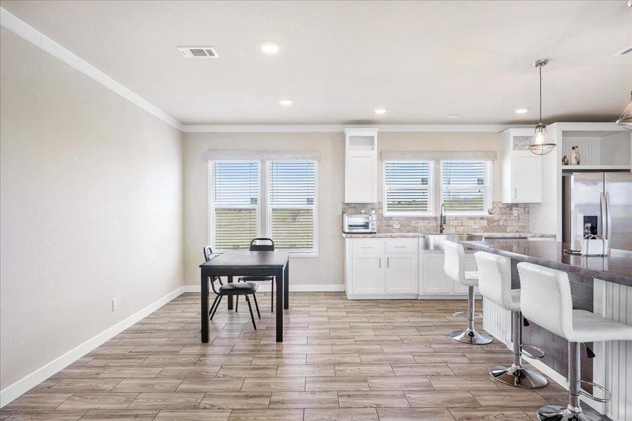 Kitchen featuring white cabinetry, wood tiled floors, stainless steel fridge with ice dispenser, a kitchen breakfast bar, and pendant lighting Kitchen featuring white cabinetry, wood tiled floors, stainless steel fridge with ice dispenser, a kitchen breakfast bar, and pendant lighting
