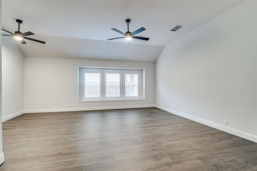 Owners suite featuring hardwood / wood-style floors, vaulted ceiling, and ceiling fan