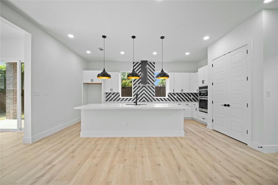 Kitchen featuring backsplash, white cabinets, light countertops, light wood-style floors, and recessed lighting