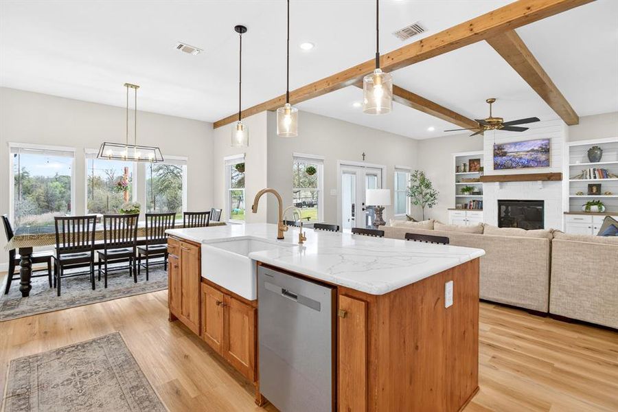 Kitchen featuring wood finish cabinetry, stainless steel dishwasher, a center island with sink, open floor plan, and pendant lighting Kitchen featuring wood finish cabinetry, stainless steel dishwasher, a center island with sink, open floor plan, and pendant lighting