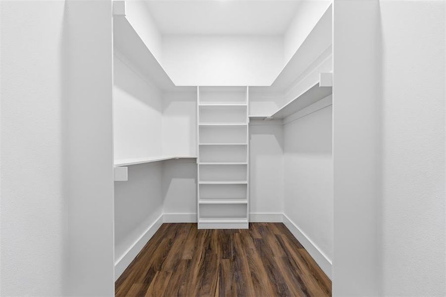 Walk-in closet featuring white built-in shelving, white walls, white baseboards, and wood-finish flooring Walk-in closet featuring white built-in shelving, white walls, white baseboards, and wood-finish flooring