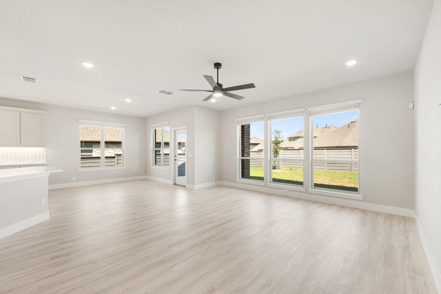 Open living room with light wood floors, ceiling fan, and large windows overlooking backyard