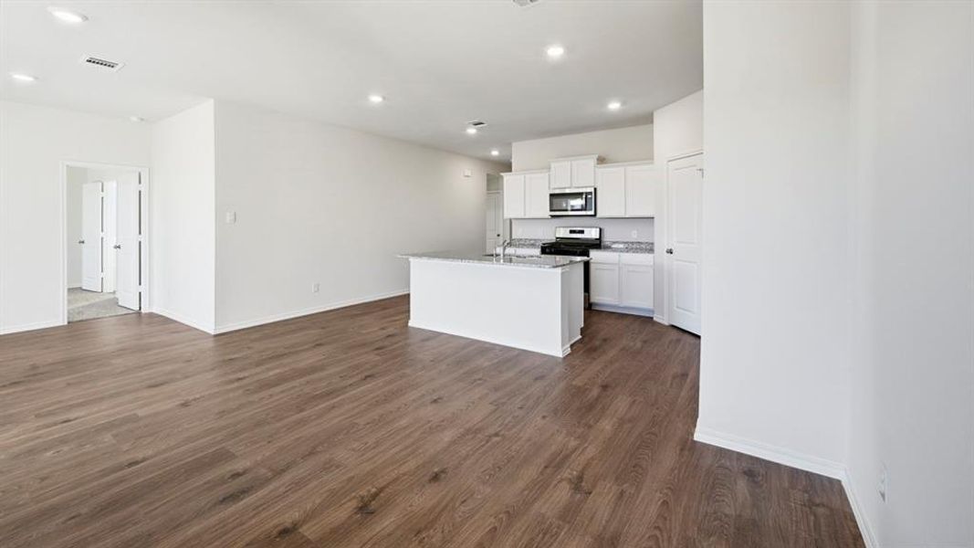 Kitchen featuring white cabinetry, an island with sink, stainless steel microwave, recessed lighting, and dark wood-style floors