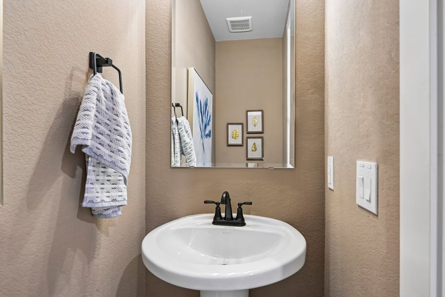 Powder room with pedestal sink, black faucet, wall mirror, and towel bar on beige textured walls