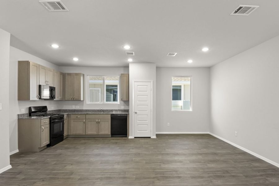 Image of a kitchen/dining area with dark vinyl flooring, a L-shaped kitchen with granite countertops and light brown cabinets