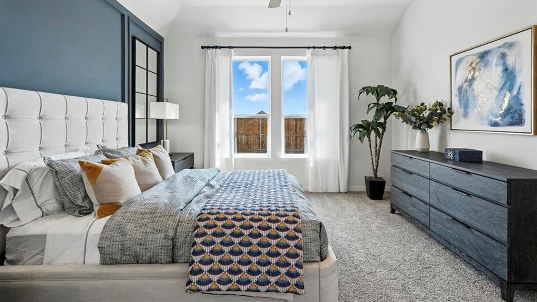 Vaulted ceiling bedroom featuring plush carpeting, a built-in paneled accent wall, two large windows with curtain rods, and a ceiling fan with integrated lighting