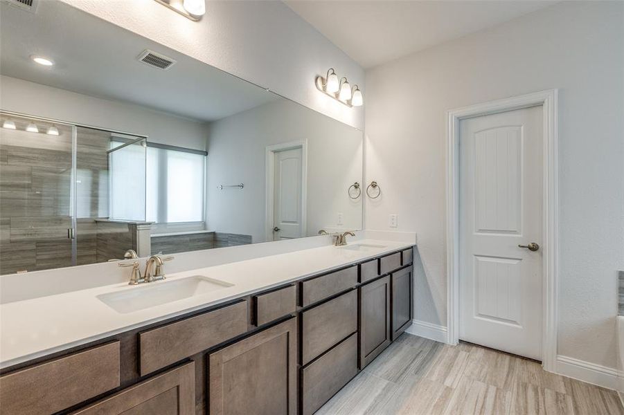 Full bath featuring double vanity, baseboards, an enclosed shower, and wood finished floors