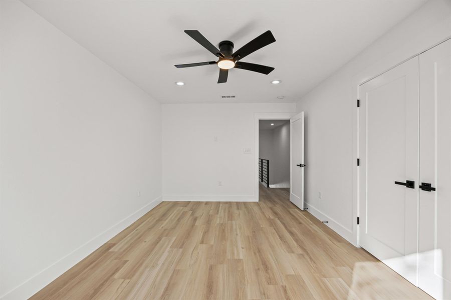 Same bedroom, different angle, featuring light wood-style flooring, recessed lighting, a ceiling fan, and a closet