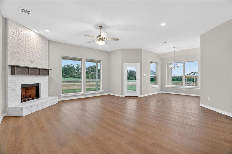 Open-concept living area featuring wood-finish flooring, a white-painted brick fireplace with a dark wood mantel, and a ceiling fan