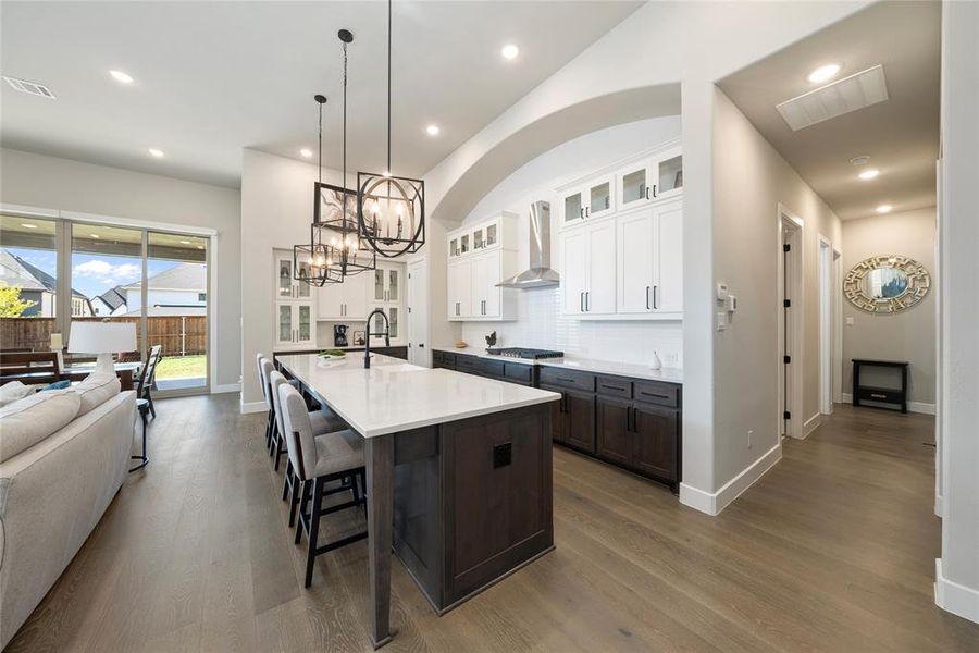 Kitchen featuring white cabinets, dark hardwood / wood-style flooring, stainless steel gas stovetop, a center island with sink, and wall chimney range hood