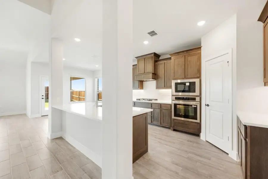 Kitchen with brown wood cabinets, stainless steel double oven, and white countertops on light tile floors