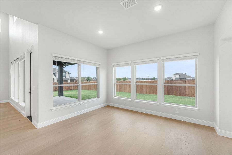 Empty room with light wood floors, large windows overlooking a fenced backyard with green lawn