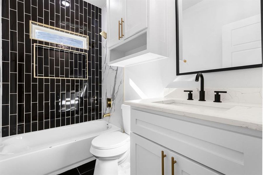 Full bathroom with tile patterned floors, tiled shower / bath combo, toilet, and vanity