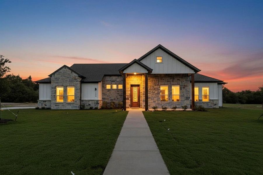 Modern farmhouse style home featuring board and batten siding, a front lawn, and stone siding