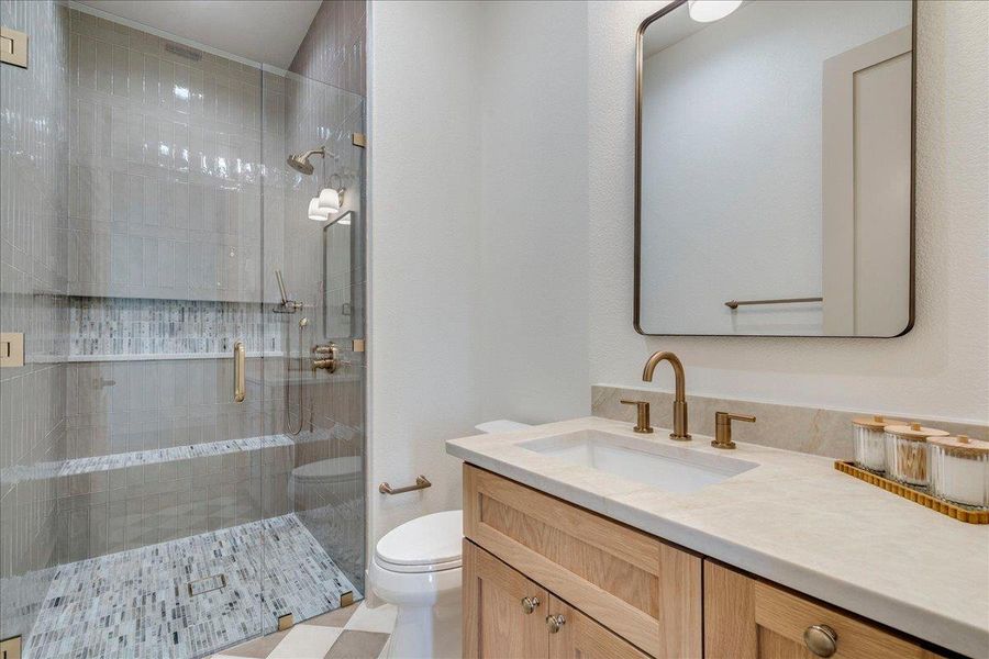 A well-appointed bathroom features a glass-enclosed shower alongside a wooden vanity with a sleek countertop.