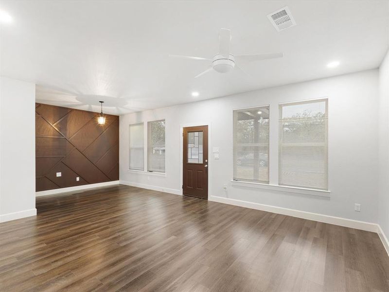 Unfurnished living room with a barn door, an accent wall, dark wood-type flooring, ceiling fan, and wooden walls