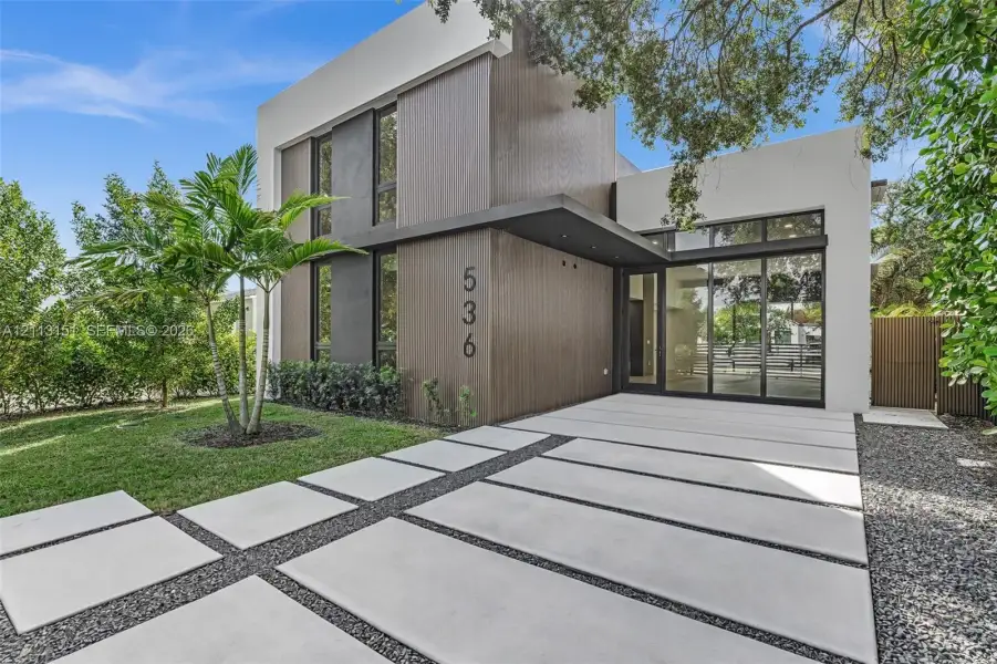Modern exterior featuring wood-finish paneling, smooth stucco finish, floor-to-ceiling glass paneling, a covered entryway, and a geometric concrete paver driveway Modern exterior featuring wood-finish paneling, smooth stucco finish, floor-to-ceiling glass paneling, a covered entryway, and a geometric concrete paver driveway