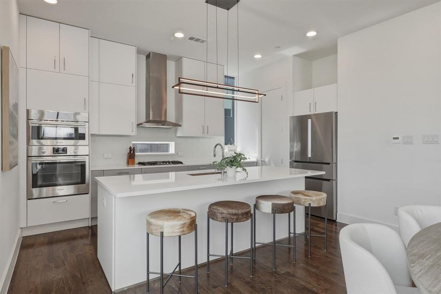 Modern kitchen featuring stainless steel appliances, white cabinetry, a large kitchen island with seating, and dark wood flooring