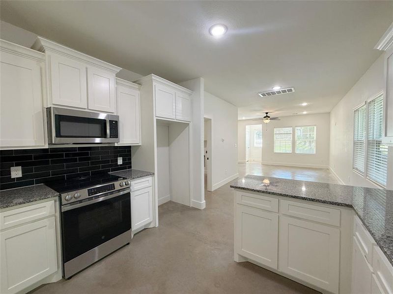 Kitchen featuring stainless steel appliances, finished concrete floors, white cabinetry, decorative backsplash, and recessed lighting