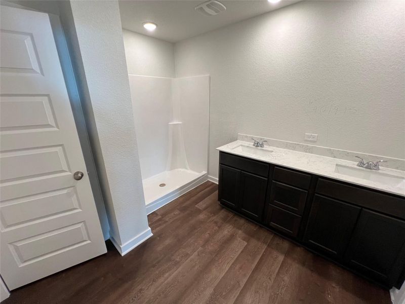 Bathroom with a textured wall, dark wood-type flooring, a shower stall, and double vanity Bathroom with a textured wall, dark wood-type flooring, a shower stall, and double vanity
