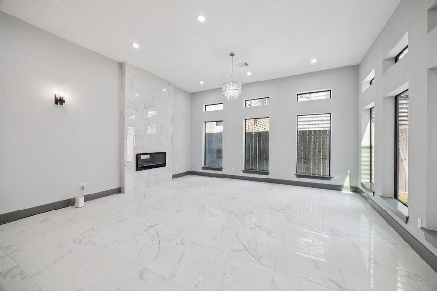 A wall of windows fills the living room with natural light, highlighting tile flooring and clean lines throughout. The modern fireplace with full-height surround adds a polished focal point, while the open layout creates flexibility for both entertaining and everyday comfort.