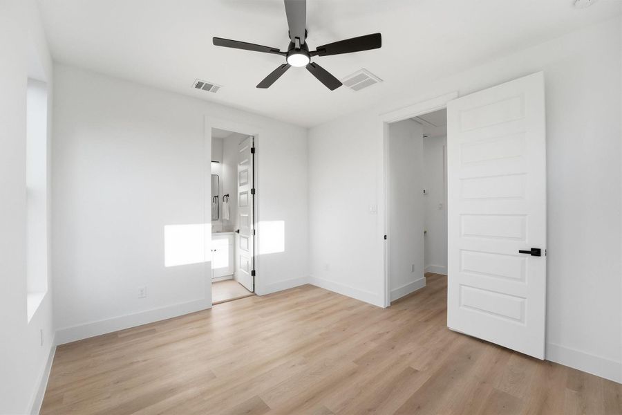 Bright and spacious bedroom featuring wood-look flooring, a modern ceiling fan, and direct access to a private ensuite bathroom, offering a clean, contemporary retreat with excellent natural light.