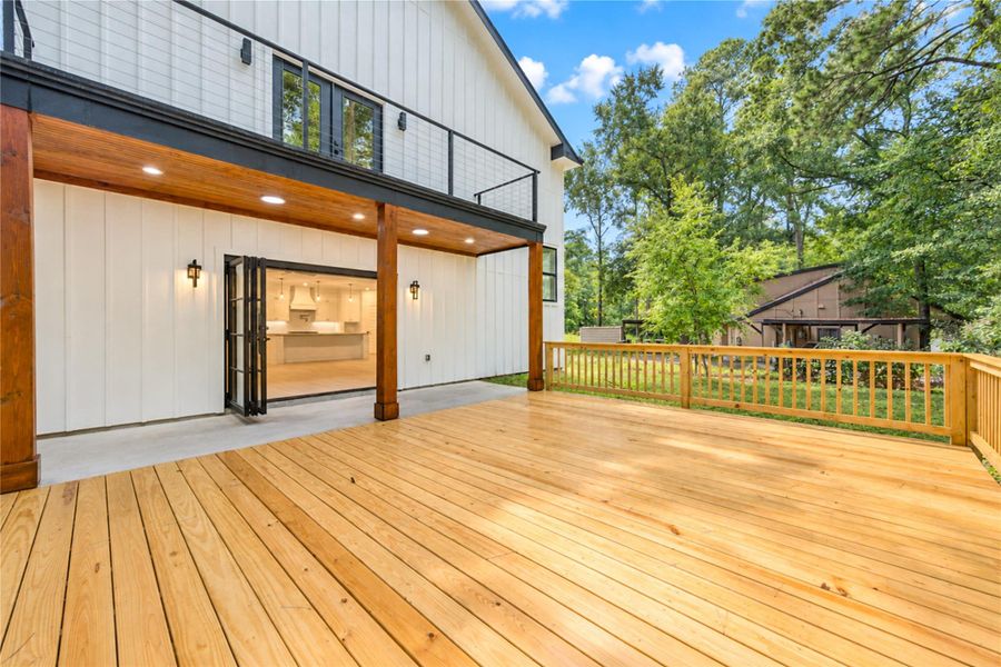 Expansive wooden deck perfect for entertaining, with a seamless indoor-outdoor flow highlighted by folding glass doors leading to a modern kitchen.