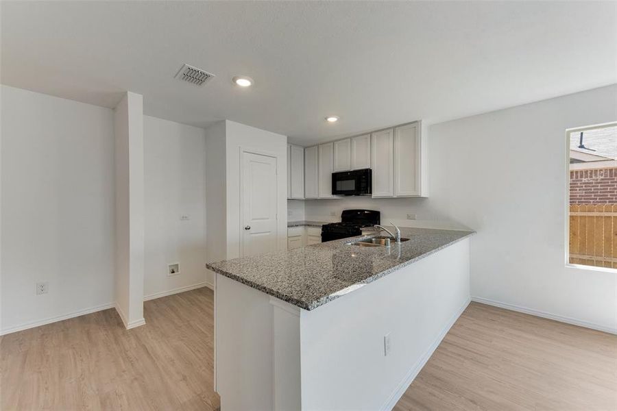 Kitchen featuring dark stone countertops, kitchen peninsula, black appliances, light hardwood / wood-style flooring, and sink