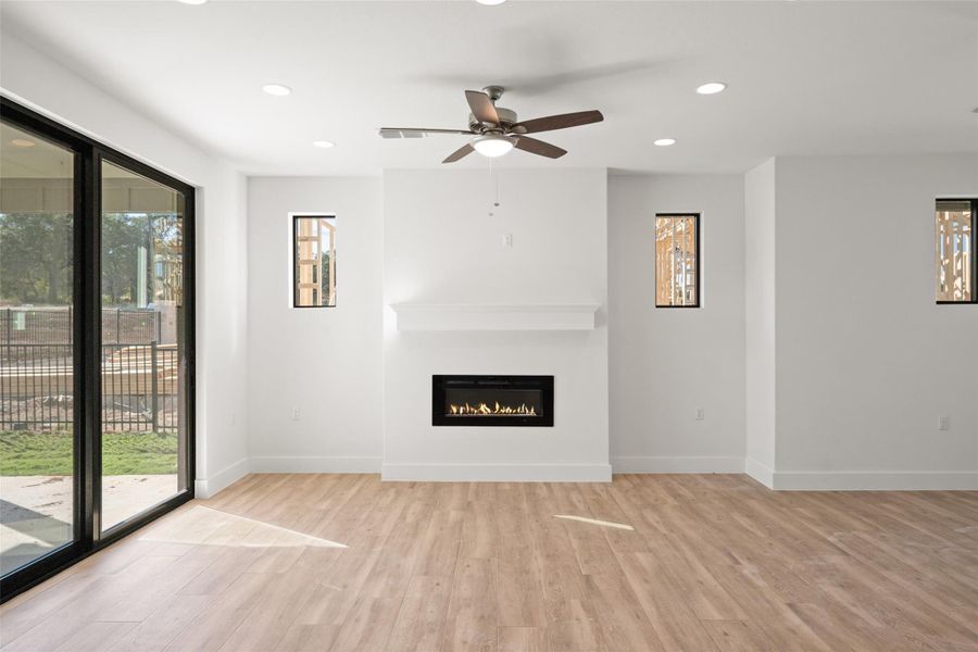 Unfurnished living room with plenty of natural light, recessed lighting, light wood-style floors, a glass covered fireplace, and a ceiling fan